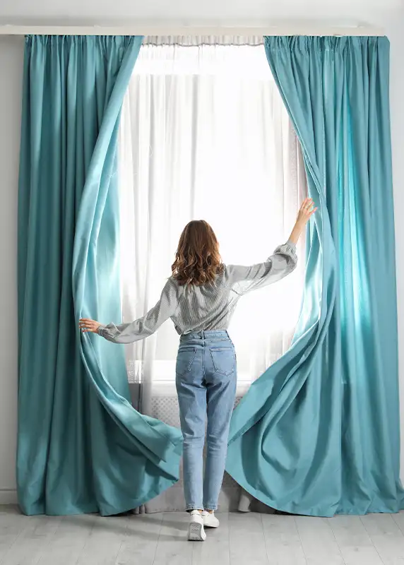 Custom teal drapery panels being opened in sunlit room, window treatment design by Ash Street Upholstery in Springfield, IL